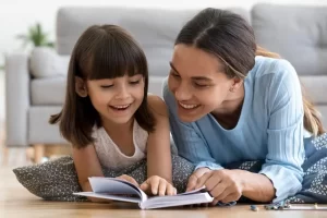 women laying on the ground reading a book to a girl