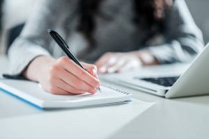female writing in notebook on desk