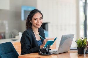 women looking at camera and smiling while at a desk with her laptop