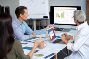 man pointing at spreadsheet to other man and women