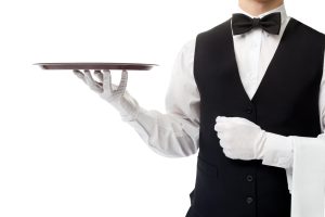 butler in black vest and white shirt holding a towel on one arm and a tray in the other hand