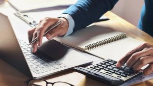 man at desk typing on laptop while typing on a calculator