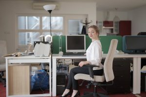 A woman sitting on a chair in front of a desk with monitors in it