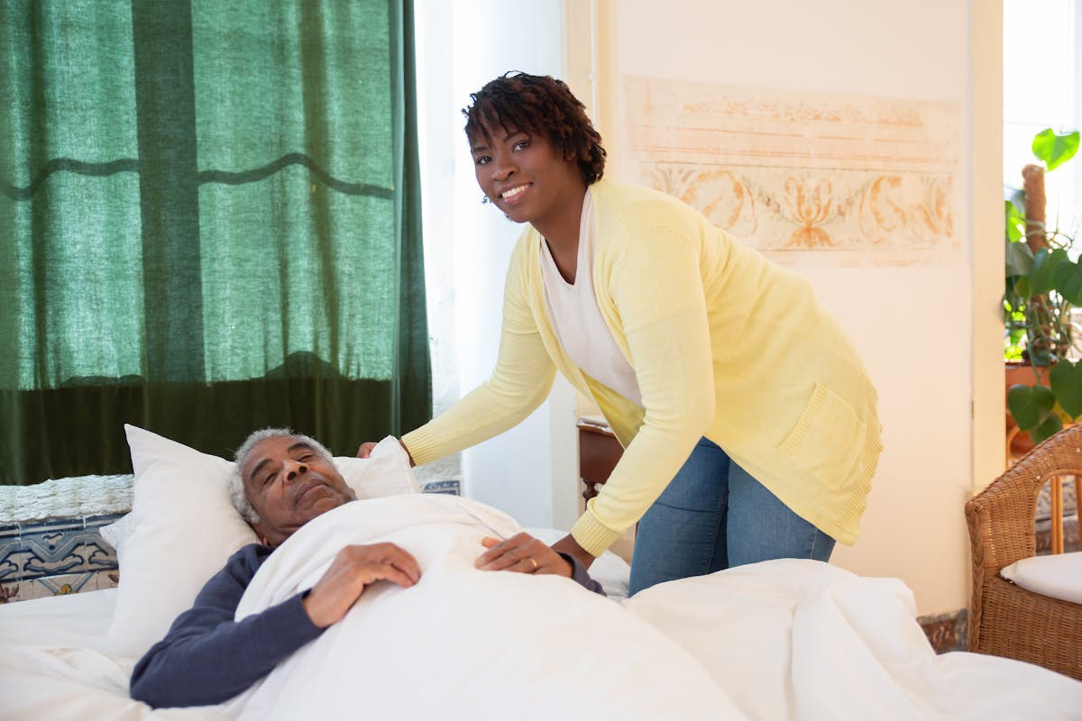 A caregiver putting an old man in a bed